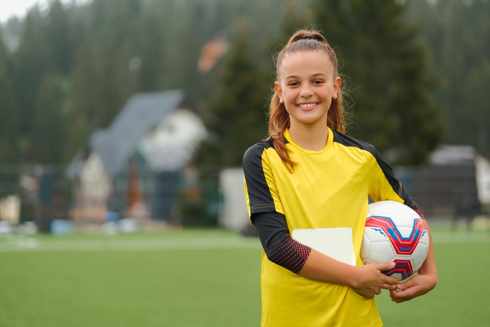 Happy female football player holding ball in her arms