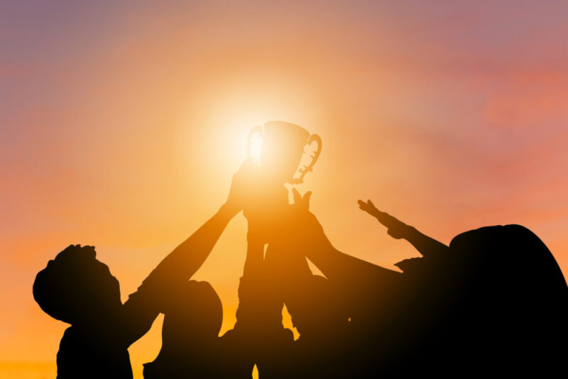 Team lifting their winning trophy in the golden light at sunset