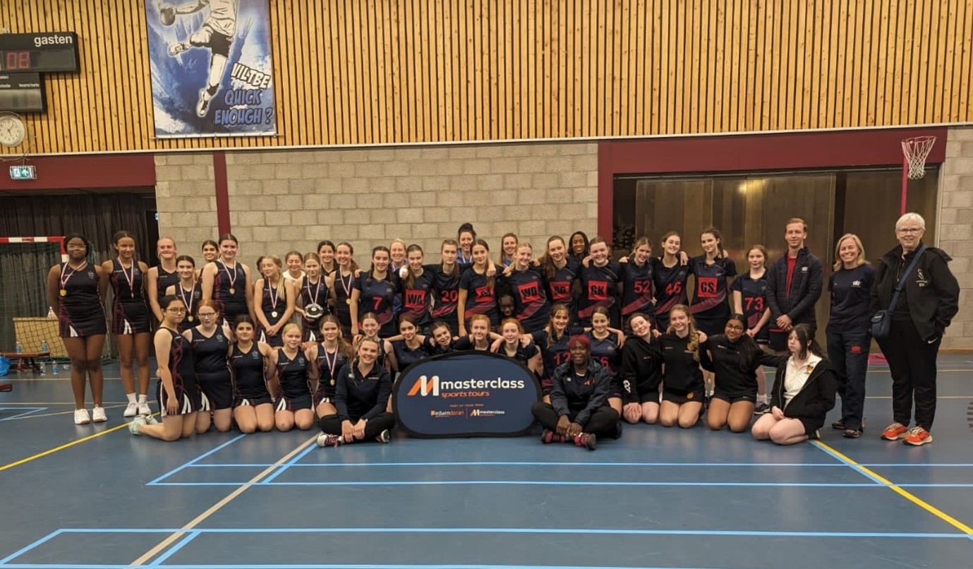 A large group of young female netballers taking a group picture together and smiling at the camera