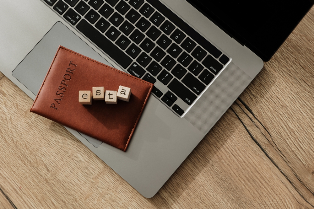 Wooden blocks spelling ESTA placed over passport and laptop