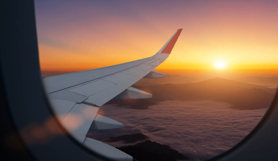 Airplane flying low over foggy mountains at sunset