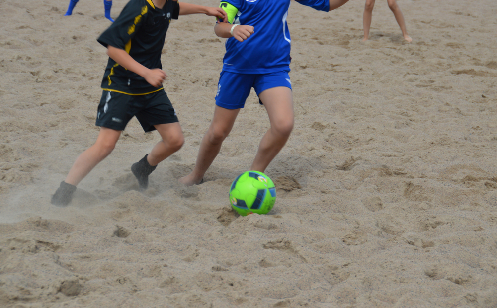 Two young boys playing football on a sandy beach