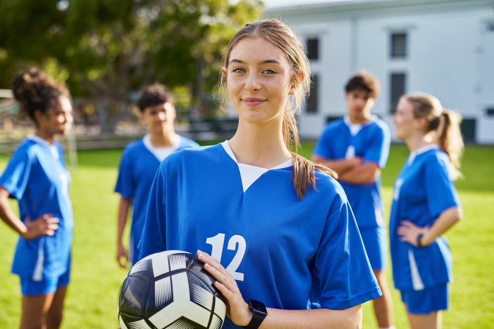 Girl from a football girls team in a blue jersey smiling at the camera