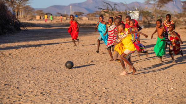 Kenyan children in colourful attire playing football in the sand