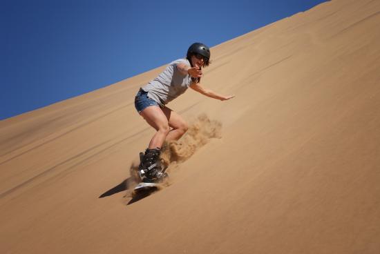 Student girl sandboarding down a dune in Namibia