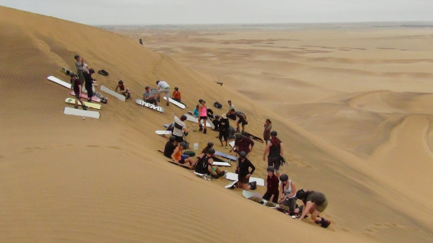 Group preparing for sandboarding from the top of a dune in Namibia